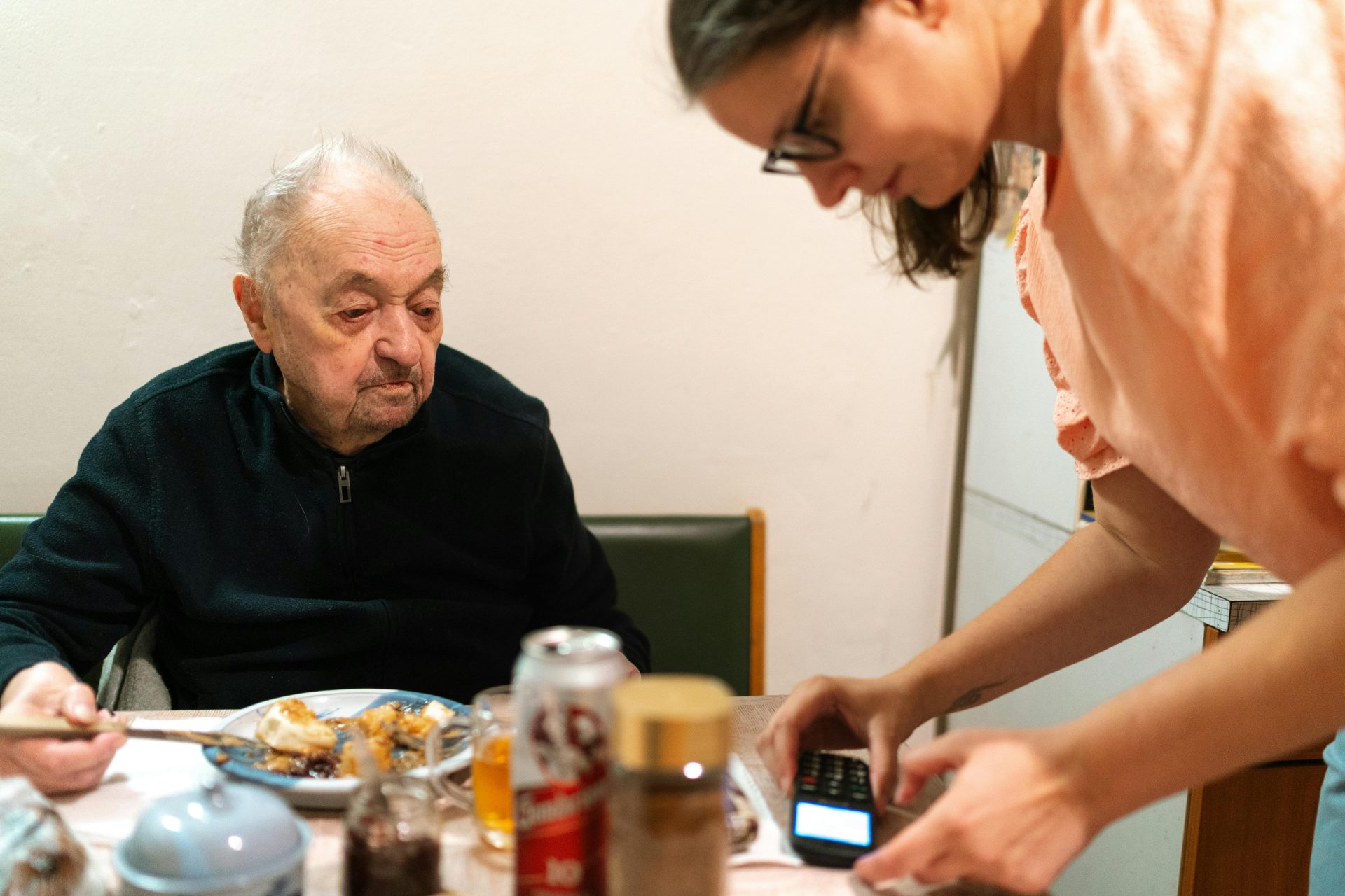 Une aide-soignante assiste un homme âgé pendant son repas, à l'intérieur d'un bâtiment. Photo prise à Prague.