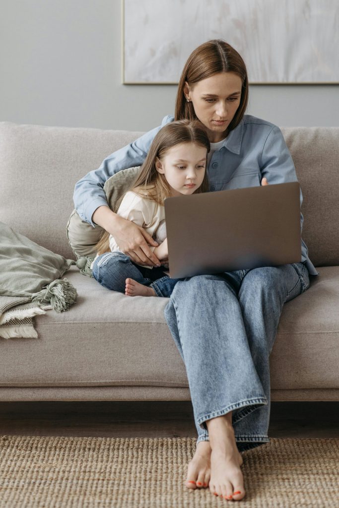 Une mère et sa fille, assises sur le canapé, utilisent ensemble un ordinateur portable et profitent d'un moment de qualité à l'intérieur.