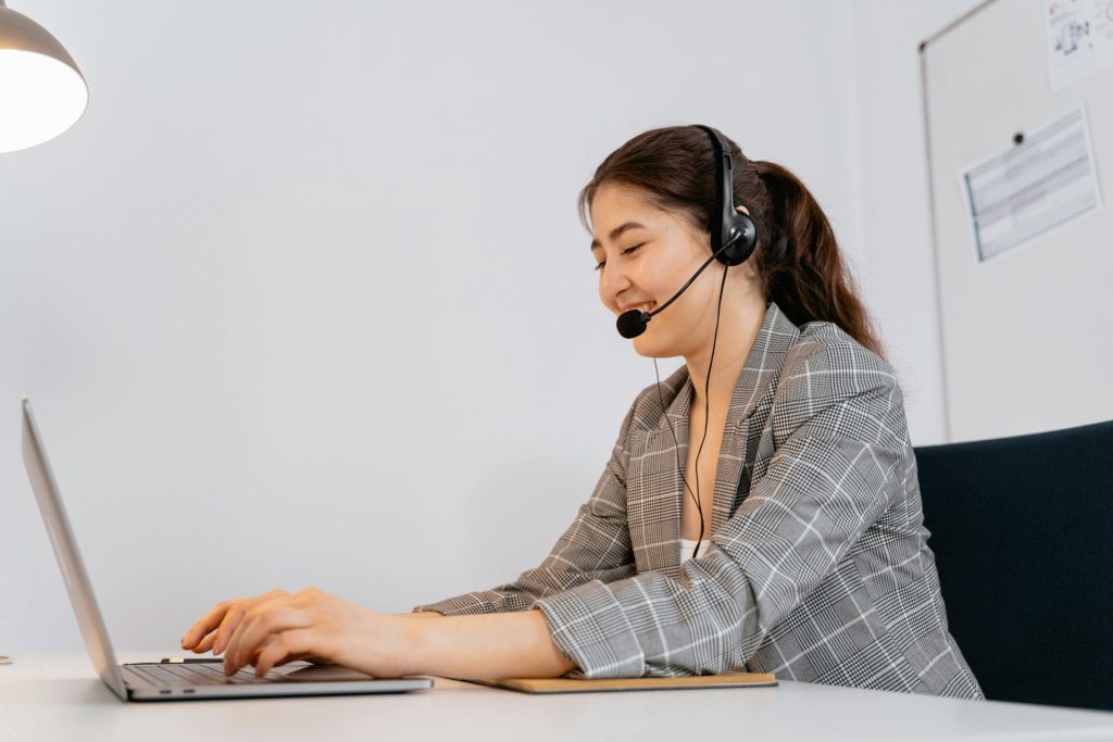 Femme en blazer à carreaux travaillant sur un ordinateur portable avec un casque audio dans un bureau.
